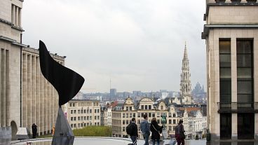 Gente paseando con equipaje con la ciudad de Bruselas como telón de fondo