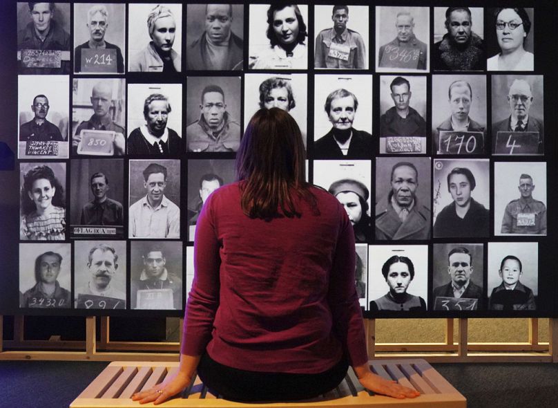 A staff member observes a digital display featuring identification photos of POWs and foreign internees, part of the 'Great Escapes' exhibition at the National Archives.
