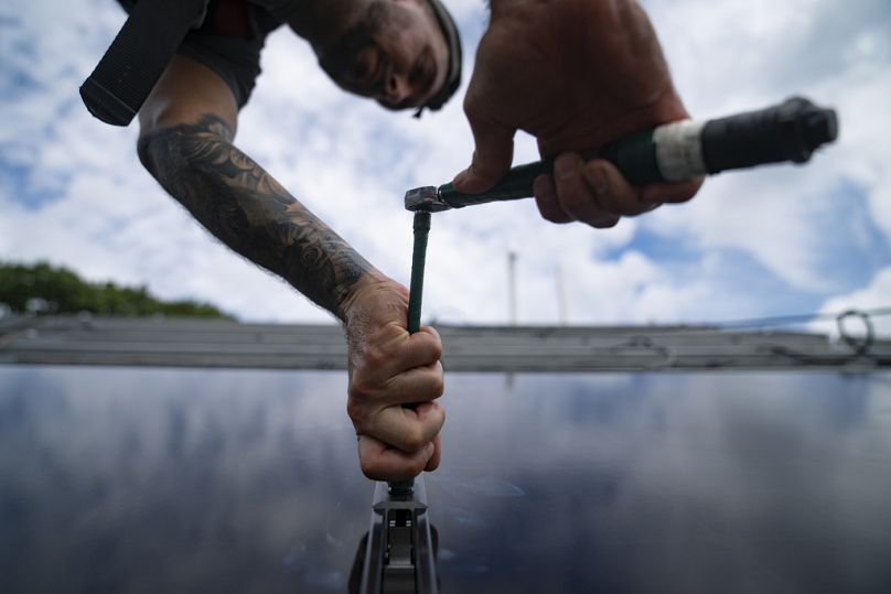 A technician installs an array of solar panels on a roof, August 2022