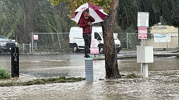 Un ciudadano se resguarda de la lluvia bajo un paraguas, en una calle inundada en Ventura, California, el domingo 4 de febrero de 2024.