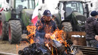 A farmer sits next to a fire during a gathering near the highway junction in Melegnano, near Milan, Italy, Wednesday, 7 February, 2024.