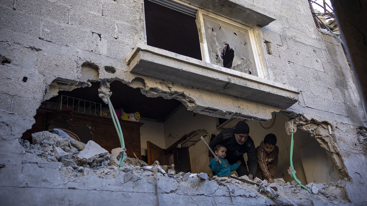Una famiglia palestinese guarda lo squarcio prodotto da un attacco israeliano a un edificio di Rafah