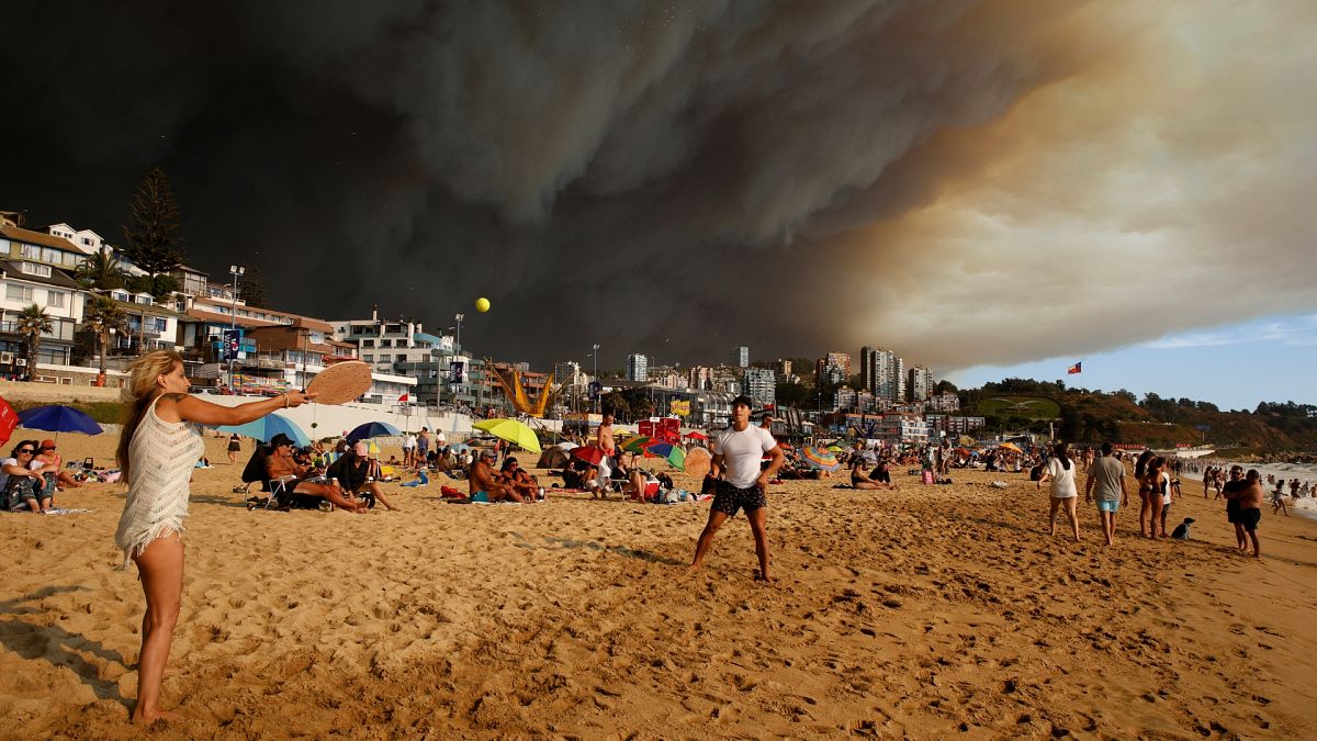 Urlauber am Strand vor dem Hintergrund eines sich verdunkelnden Himmels, der durch den Rauch der nahe gelegenen Waldbrände in Viña del Mar, Chile, verursacht wird.