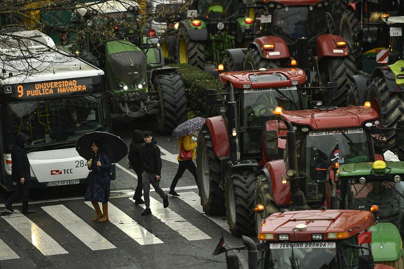 Fußgänger überqueren die Straße, während Landwirte mit ihren Traktoren durch das Stadtzentrum fahren, um an einer Protestkundgebung teilzunehmen, Pamplona, Februar 2024