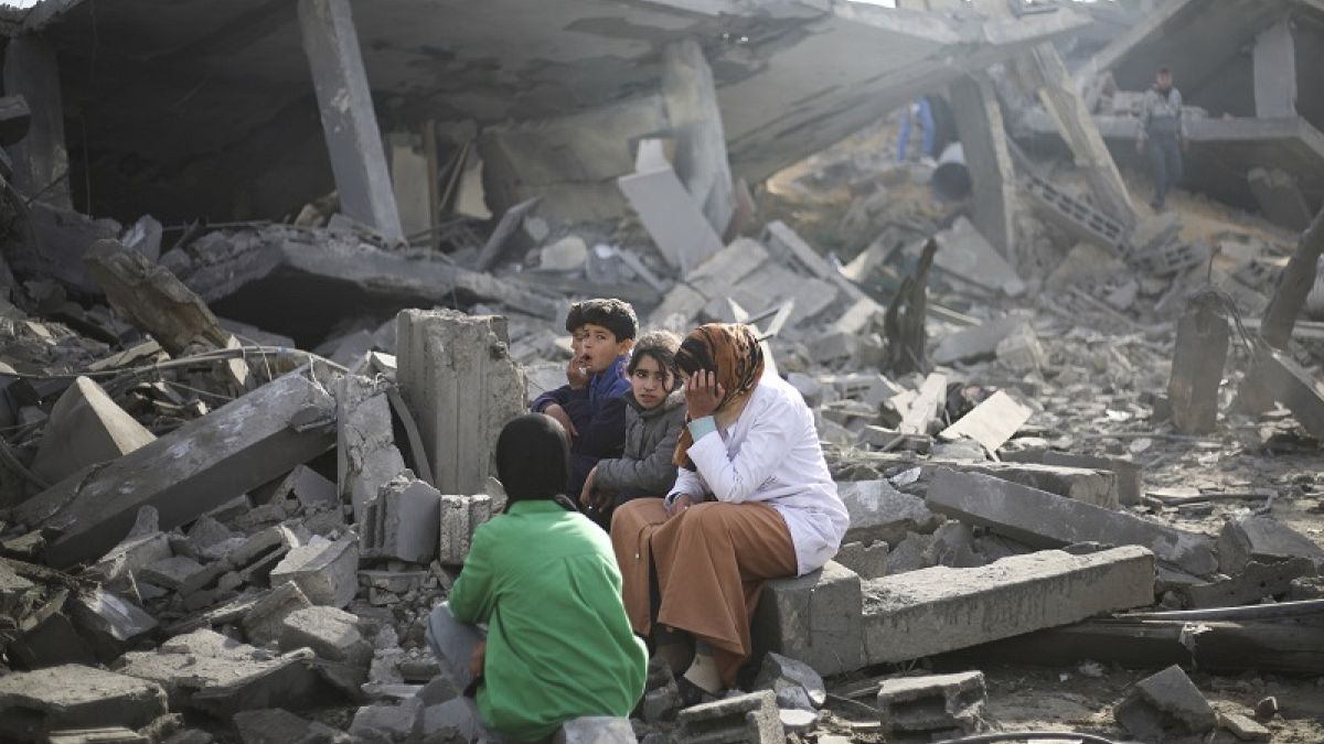 Los palestinos sentados junto a la destrucción causada por el bombardeo israelí de la Franja de Gaza en Rafah el lunes 12 de febrero de 2024.