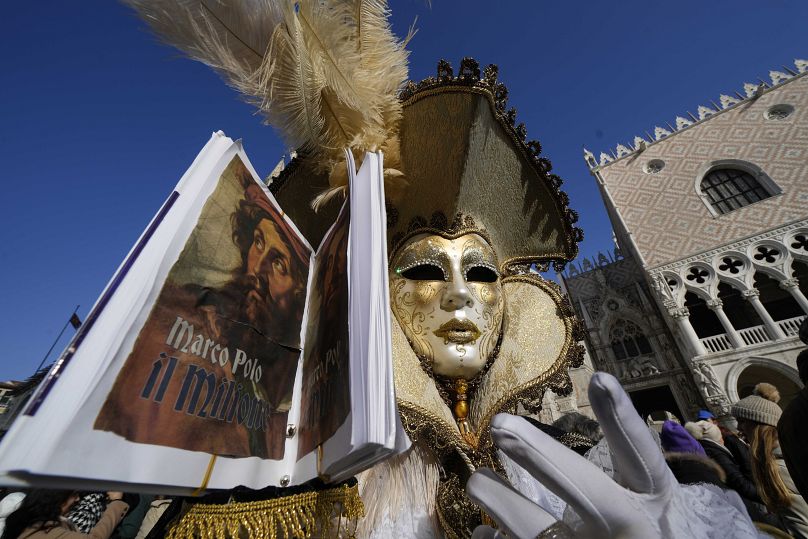 Мужчина в маске с копией книги "Миллион" - отчета о путешествиях Марко Поло по Азии на карнавале в Венеции, 28 января 2024 г.
