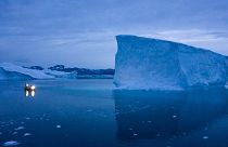  A boat navigates at night next to large icebergs in eastern Greenland. 