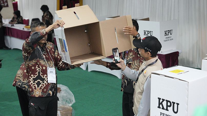 Electoral workers show an empty ballot box as the polling station opens during the election in Bojong Koneng