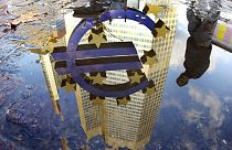 In this Thursday, Jan. 5, 2012 file photo, a person is reflected in a puddle alongside the Euro sculpture in front of the European Central Bank in Frankfurt, Germany.