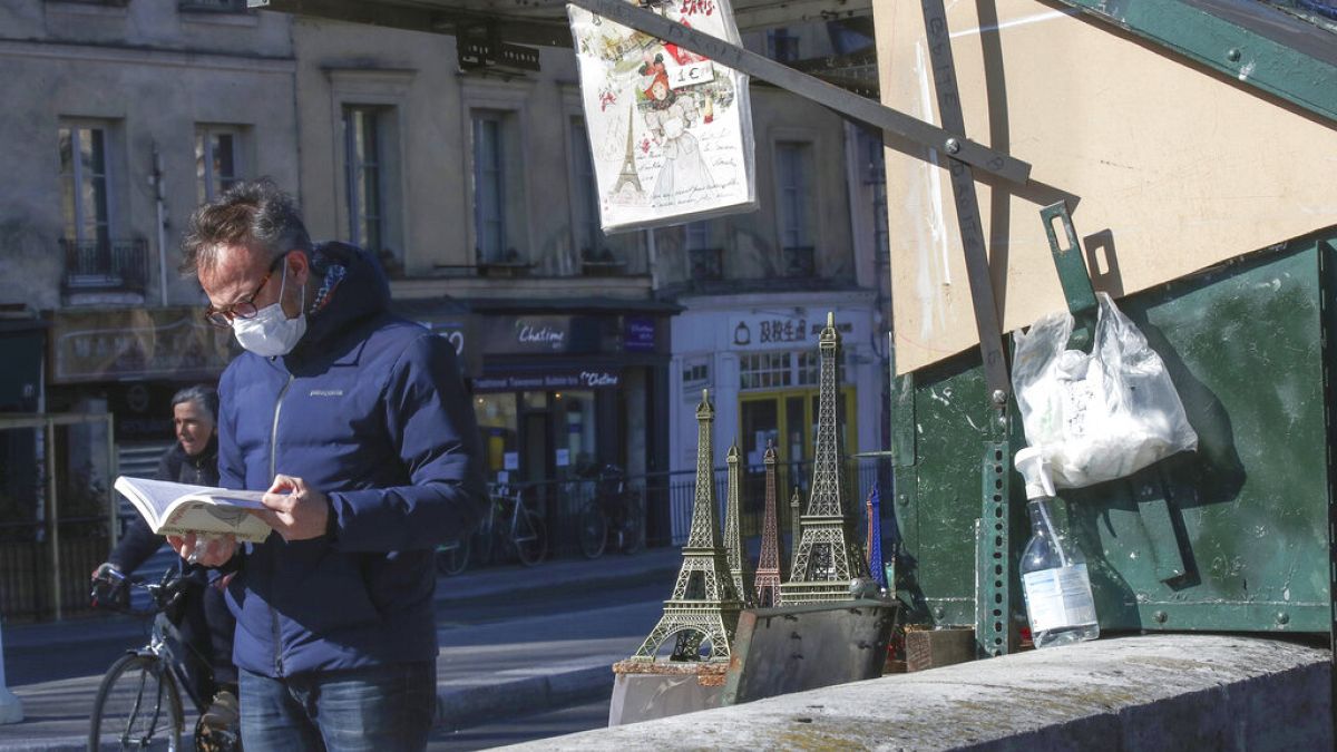 Imagen de un ciudadano ojeando un libro junto a un puesto de venta de libros de segunda mano, en una de las orillas del río Sena, en París.