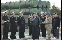 الزعيم الكوري كيم جونغ أون مع رجال يرتدون زي البحرية والجيش، ومركبة تطلق صاروخاً.