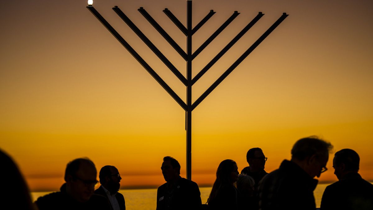 La gente se reúne alrededor de la menorá durante la "Hanukkah en el muelle" en San Clemente, California, el domingo 18 de diciembre de 2022.
