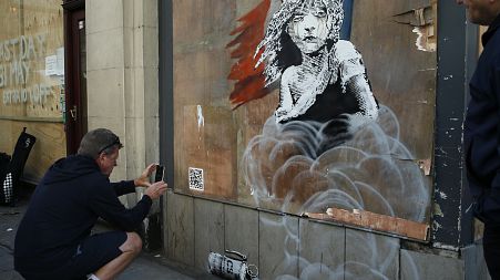 Trkač se zaustavlja kako bi svojim telefonom fotografirao novo umjetničko djelo britanskog umjetnika Banksyja nasuprot francuskog veleposlanstva, u Londonu, 2016.