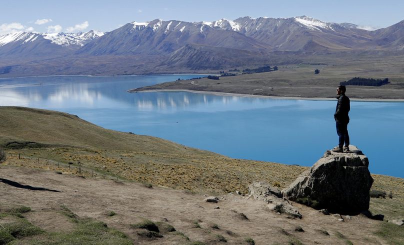 a tourist stands on a rock as he looks over Lake Tekapo and the Southern Alps in New Zealand, October 2018