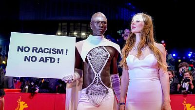 A person holds a sign reading " no racism, no AFD" on the red carpet outside the Berlinale Palast during the opening of the International Film Festival, Berlinale.