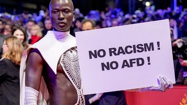Протестующий держит плакат "Нет расизму! Нет "Альтернативе для Германии!"" на красной дорожке Берлинале, 15 февраля 2024