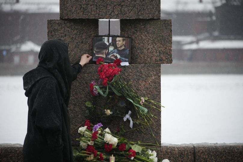 St Petersburg'daki Siyasi Baskı Kurbanları Anıtı'nda Alexey Navalny'yi anmak için çiçek bıraktıktan sonra muhalifin otoğrafına dokunan bir kadın