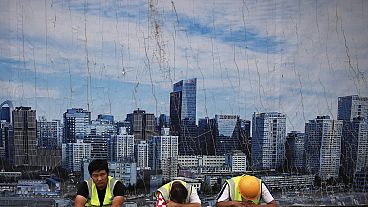 Chinese workers take a break outside a construction site wall depicting the skyline of the Chinese capital at the Central Business District in Beijing, Tuesday, June 26, 2018.