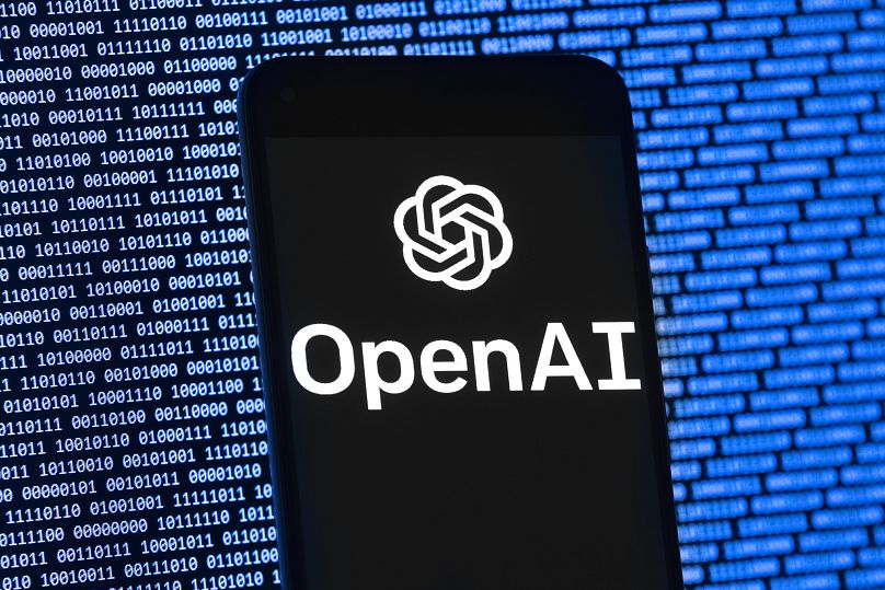 El logotipo de OpenAI aparece en un teléfono móvil frente a una pantalla de computadora con datos binarios aleatorios, el 9 de marzo de 2023