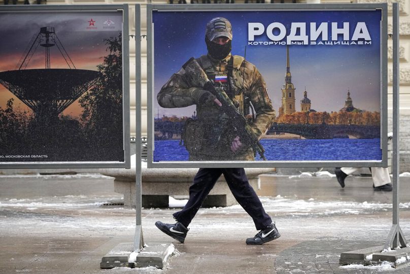 A man walks past a stand with an image of a Russian serviceman at a street exhibition of military photos in St. Petersburg, February 2023
