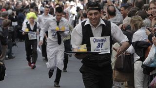 Des personnes habillées en serveurs portent des plateaux de boissons alors qu'elles participent à une course dans les rues de Paris.