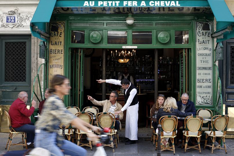Le serveur Didier Hubert, au centre, indique une direction à un client du café "Au petit Fer à Cheval", dans le quartier historique du Marais à Paris.