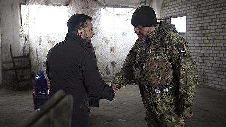 O Presidente ucraniano Volodymyr Zelenskyy, à esquerda, aperta a mão a um soldado durante a sua visita à cidade de Kupiansk, na região de Kharkiv, na Ucrânia, a 19 de fevereiro de 2024.