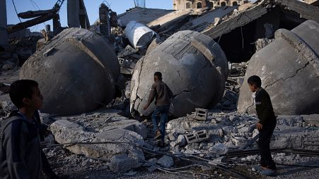 فتية فلسطينيون يمشون فوق أنقاض بيوت ومسجد في رفح دمرها القصف الإسرائيلي