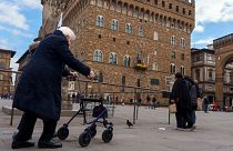 An elderly woman uses a walking frame to ambulate in front of the 14th-century town hall 'Palazzo Vecchio' (Old Palace) in Florence, Italy, Thursday, Feb. 17, 2022. 