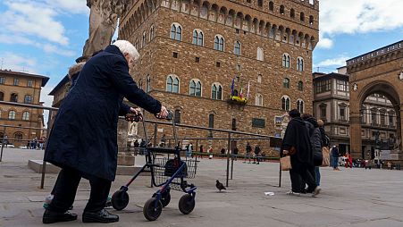 Uma mulher idosa usa um andarilho para se deslocar em frente ao Palazzo Vecchio (Palácio Velho) da Câmara Municipal do século XIV em Florença, Itália, quinta-feira, 17 de fevereiro de 2022. 