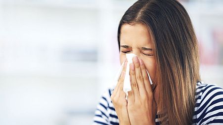 A person suffering from allergies blows their nose.