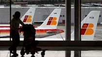 Des avions d'Iberia sont vus dans une zone de stationnement alors qu'une passagère porte ses bagages.