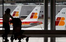 Iberia jets are seen in a parking zone as a passenger carries her luggage.