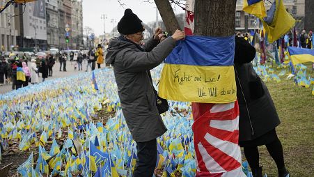 متطوع ياباني يعلق علم أوكرانيا على شجرة في ساحة ميدان بالعاصمة كييف في الذكرى الثانية للحرب الروسية الأوكرانية