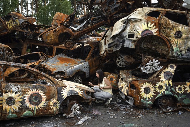 A Ukrainian artist Olena Yanko paints sunflowers on cars which were destroyed by Russian attacks in Irpin, August 2022