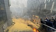 La gente mira por un balcón mientras arden incendios y se esparce heno en la calle durante una protesta de agricultores en Bruselas, el 26 de febrero, 2024.