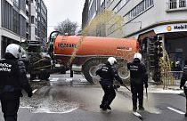 Фермер разбрасывает из цистерны навоз перед учреждениями Евросоюза в Брюсселе. Приближаются полицейские в касках.