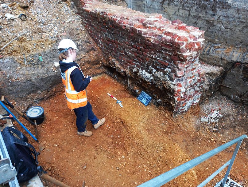 Ein Archäologe dokumentiert eine große nachmittelalterliche Mauer, die ausgegraben wurde.