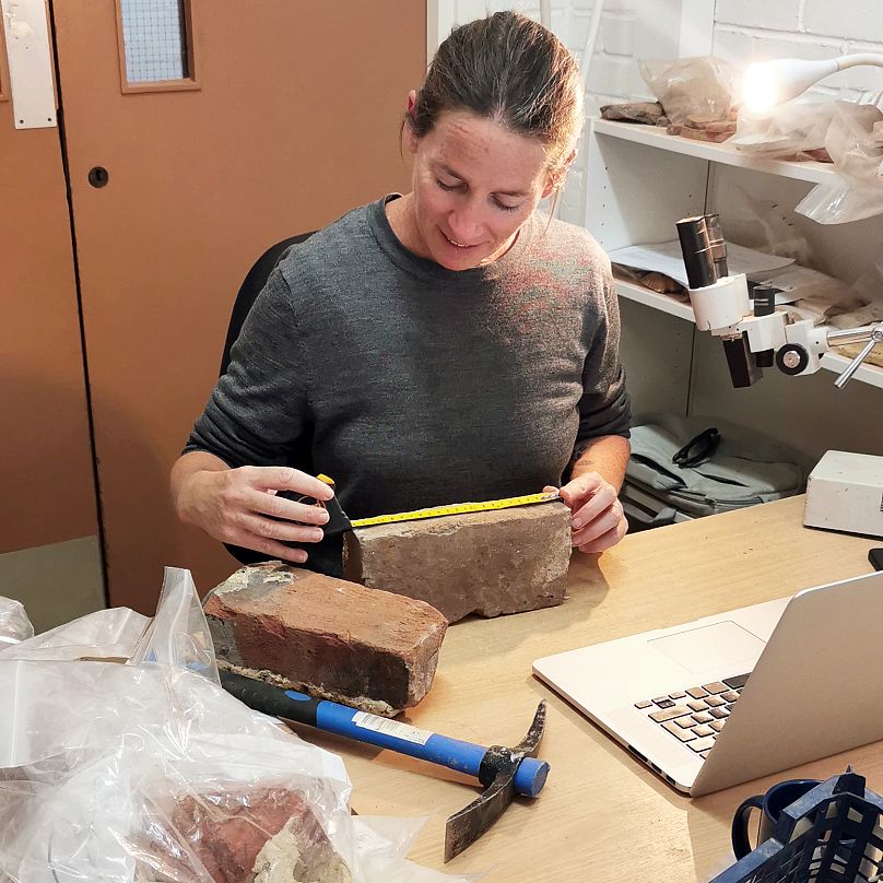 Rae Regensberg, die Spezialistin für keramische Baustoffe bei Archaeology South-East, betrachtet Ziegel aus der Ausgrabungsstätte.