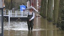 A woman carries a chair on her head as she walks in a flooded street of Arques, northern France, Thursday, Jan.4, 2024. 