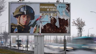 Carros passam por um painel publicitário em São Petersburgo que promove o serviço militar contratado no exército russo.