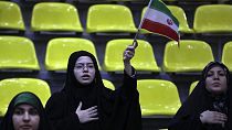 Iranian women listen to their country's national anthem as one of them waves the national flag during an election campaign rally ahead of the March 1, parliamentary and Assemb