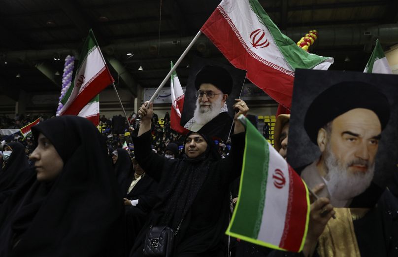 Iranian women at an election rally wave posters of the Supreme Leader Ayatollah Ali Khamenei and the late revolutionary founder Ayatollah Khomeini