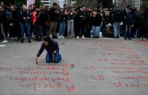 شابة تكتب أسماء ضحايا كارثة السكك الحديدية قبل عام واحد، أمام البرلمان اليوناني