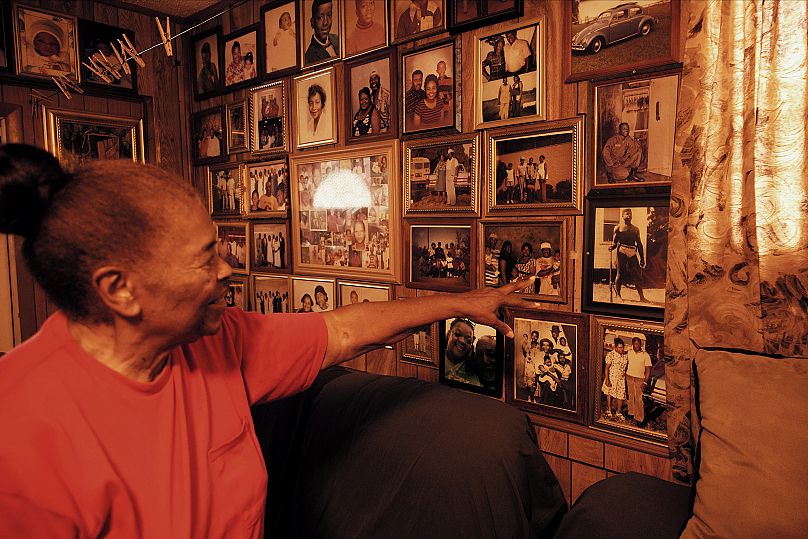 Ms. Daisy pointing to photographs on the wall in her home.