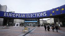 Des personnes marchent sous une bannière annonçant les élections européennes devant le Parlement européen à Bruxelles.