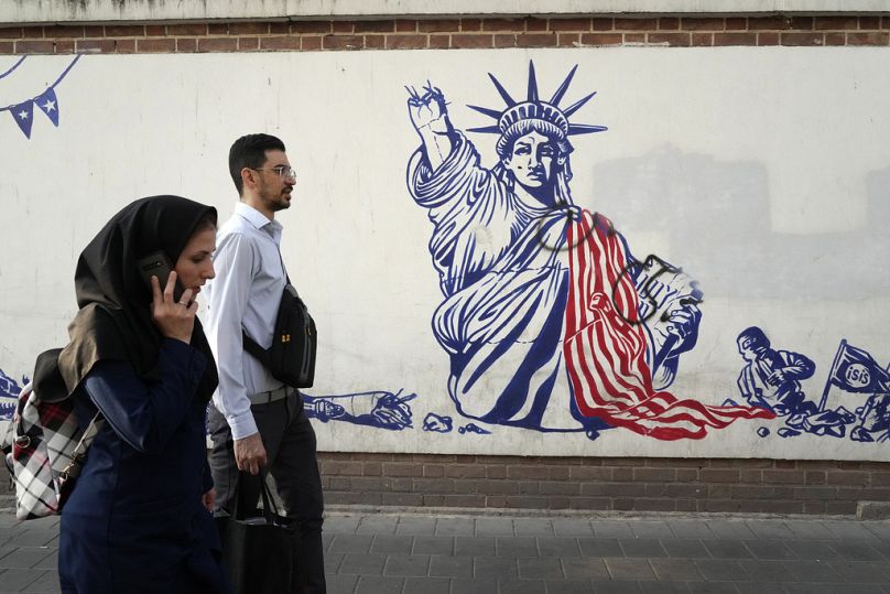 People walk past an anti-US mural painted on the wall of the former U.S. Embassy in Tehran, August 2023