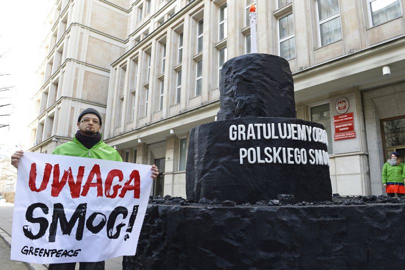 An activist holds a banner reading "Attention Smog" next to an installation resembling a cake made of coal in front of the Energy Ministry, in Warsaw, February 2018