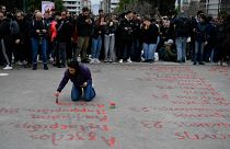 A young woman paints the name of victims from a rail disaster one year ago, in front of parliament, in Athens, Greece, Wednesday, Feb. 28, 2024. 