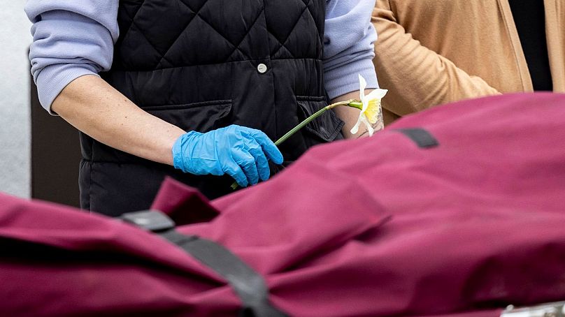 A caregiver holds a daffodil in front of a stretcher on which a deceased person is being carried outside a retirement home after a fire broke out during the night.